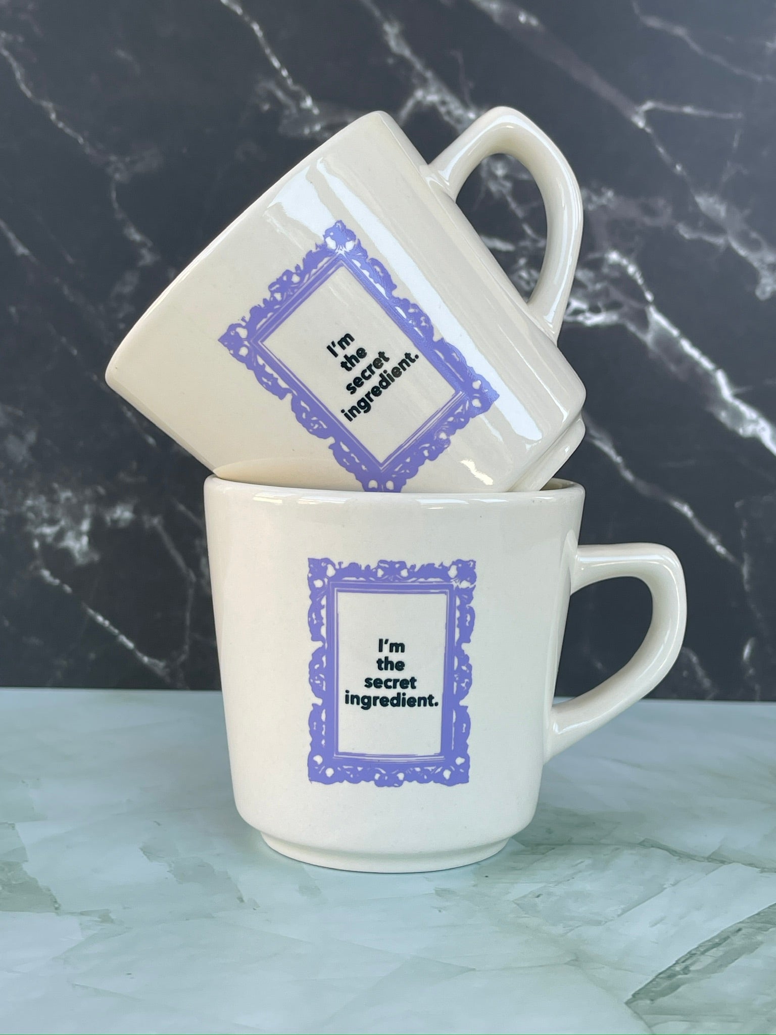Two TruCrumb white mugs with purple text on a marble surface